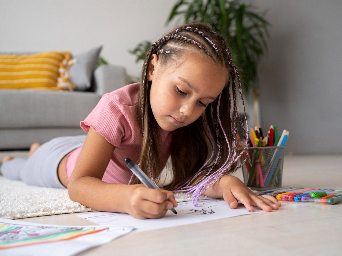 A girl lying on the floor, drawing on a sheet of paper