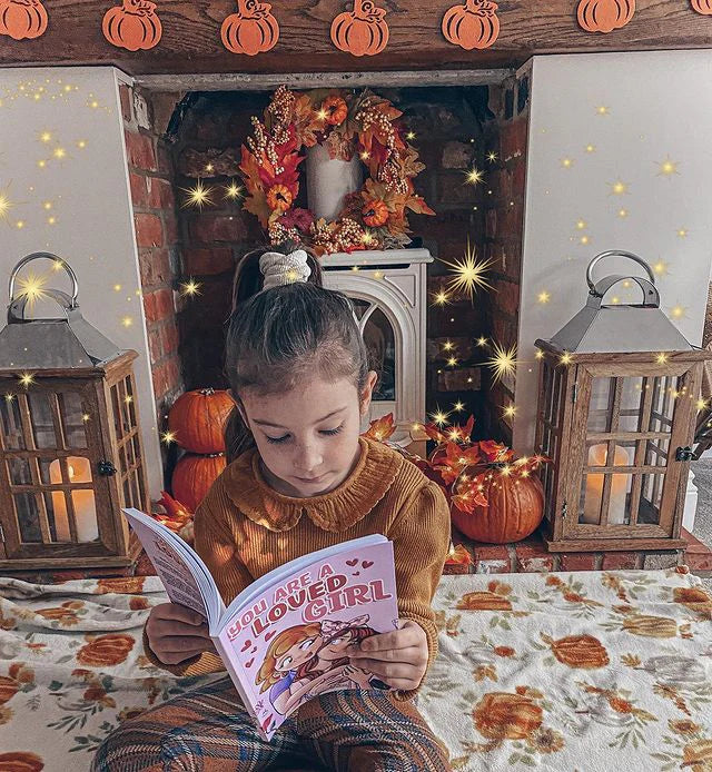 A girl reading You Are a Loved Girl among autumn decorations
