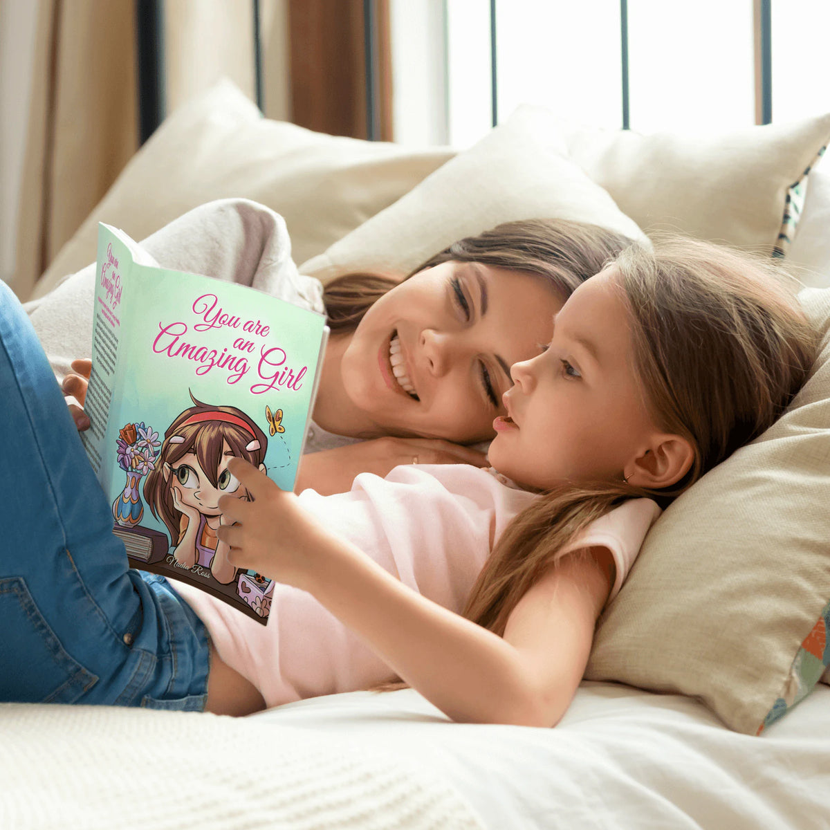 A girl and a grown-up read You Are an Amazing Girl together in bed, smiling.