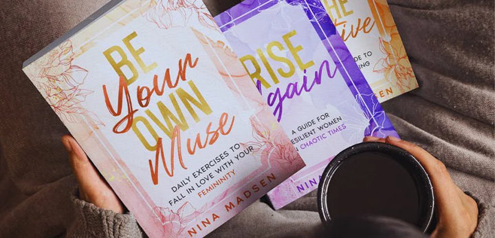 Hands holding Be Your Own Muse and Rise Again, with a cup of coffee