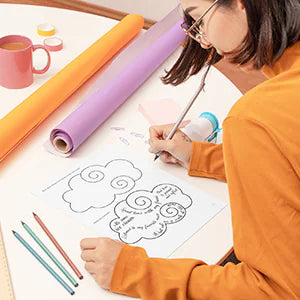 A woman colors a hand-lettered page with colored pencils.
