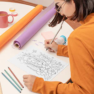 A woman colors a floral lettering page with colored pencils.