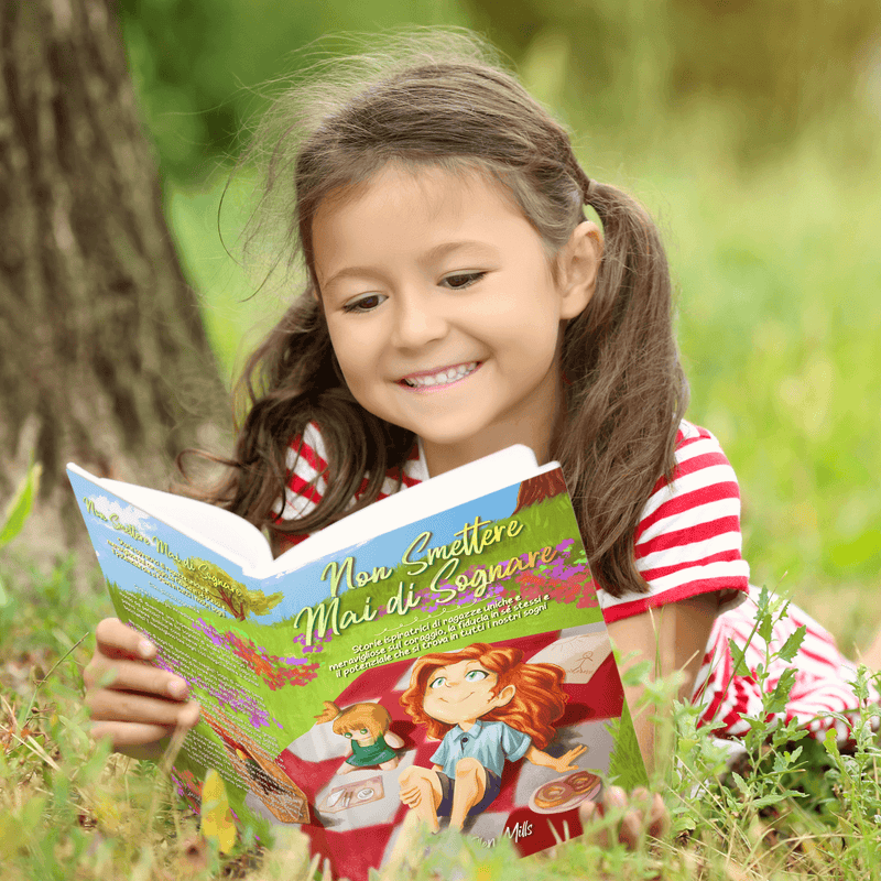 Una bambina sorridente, sdraiata nell’erba, legge Non smettere mai di sognare.