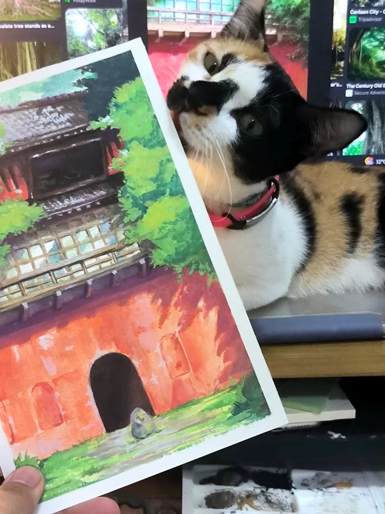 A painting by Ren Ebit, a red temple among green trees, held up next to a calico cat